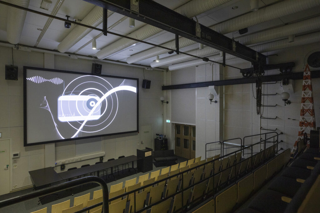 Yleiskuva Mastolan uudistetusta auditoriosta. Vasemmalla nähtävissä auditoriossa esitettävä Mastolan introvideo.