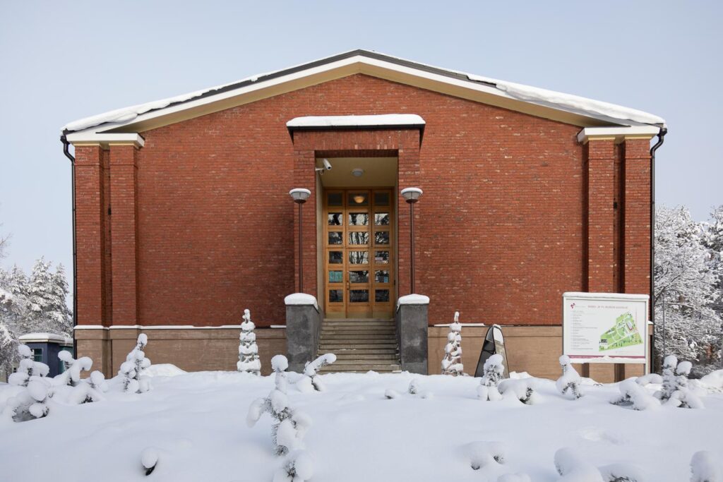 Talvinen kuva museorakennuksesta. Punatiilisen rakennuksen pääsisäänkäynti lumisessa maisemassa.